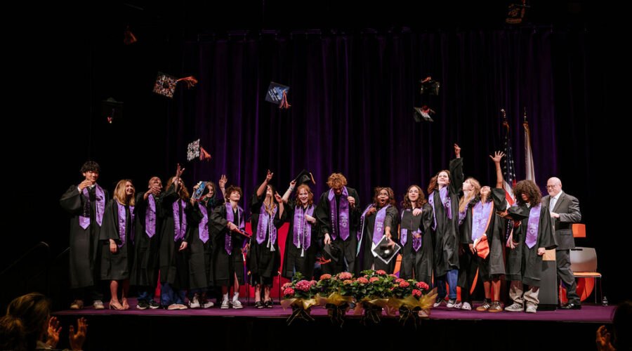 New England Innovation Academy graduates tossing caps on stage at commencement
